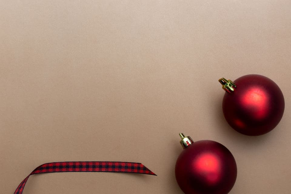 Two red Christmas baubles and a tartan ribbon on a plain background